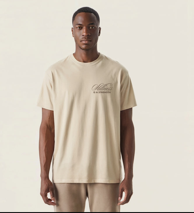 Male model wearing a neutral sandstone oversized T-shirt with the words ‘Stillness Is a Strength’ printed on the left chest, minimalist design by 19-89 Haute.